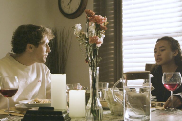 Still from Tuesday: a couple seated across from each other at a dinner table
