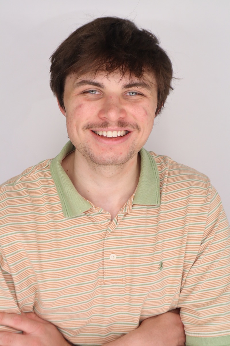 Owen Keller smiling in a striped green and orange polo against a light gray backdrop
